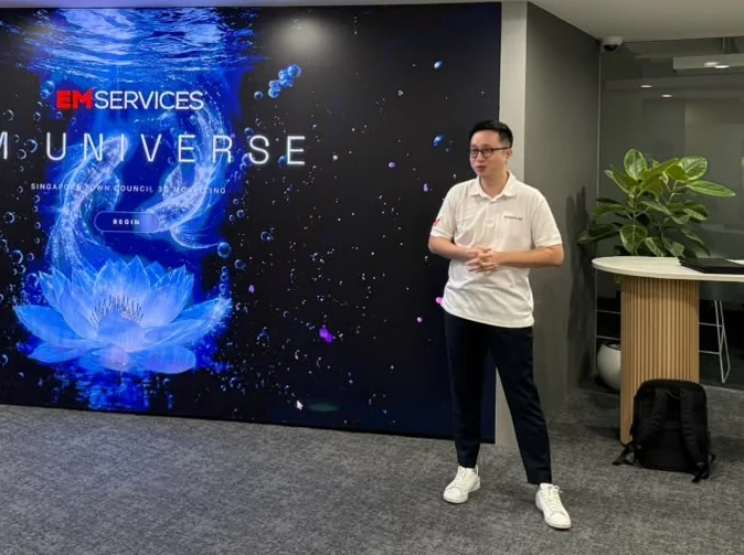 A presenter standing beside a large EM Services digital display